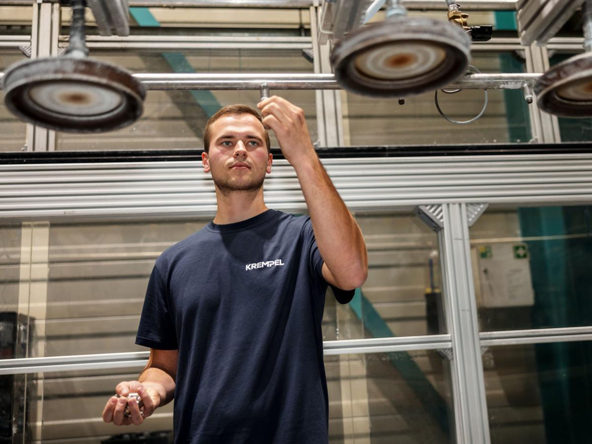 Young man is standing in a production area and working on a machine