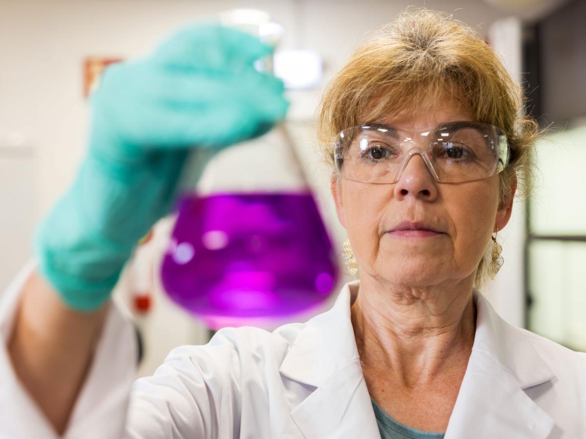 Woman holding a chemical glass with pink liquid inside and looking into it